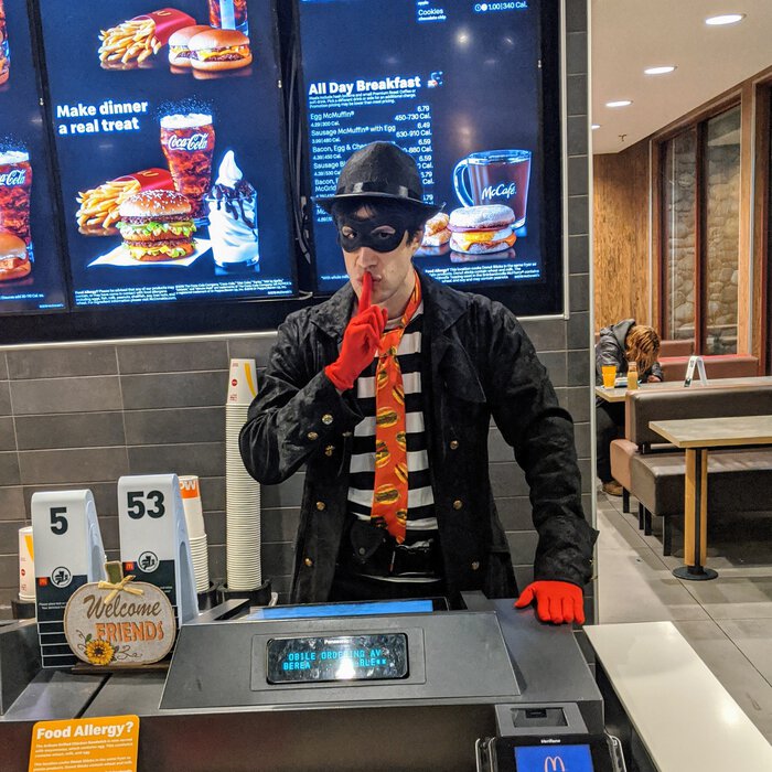 Pablo dressed as the Hamburglar, behind the counter at a McDonalds, looking mischevious. Click for full size.