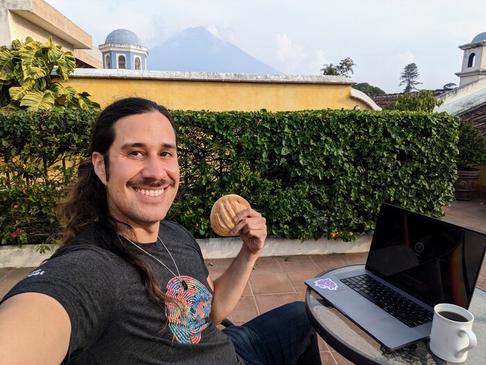 Pablo, holding a pan dulce, in Guatemala with a volcano behind him.